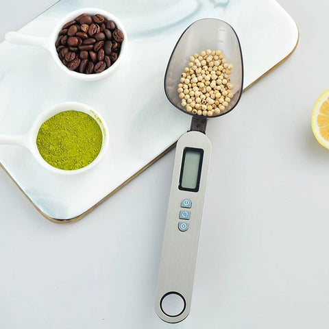 Bilancia cucchiaio digitale Kiwi con display LCD che pesa legumi accanto a caffè e tè matcha, ideale per dosare ingredienti con precisione in cucina e pasticceria